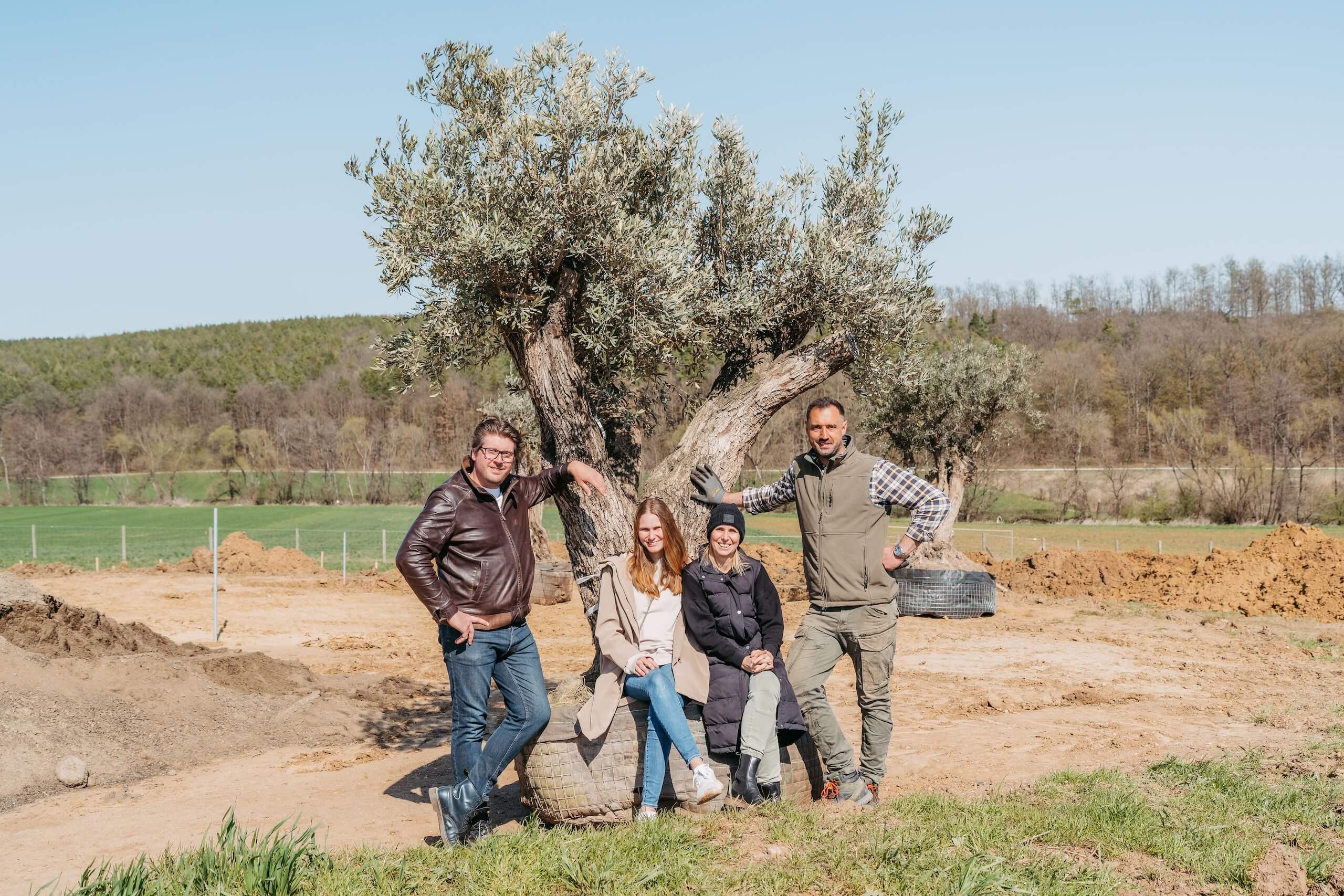 Gruppe von Menschen posiert vor einem großen Olivenbaum auf einer idyllischen Hochzeitslocation im Freien.