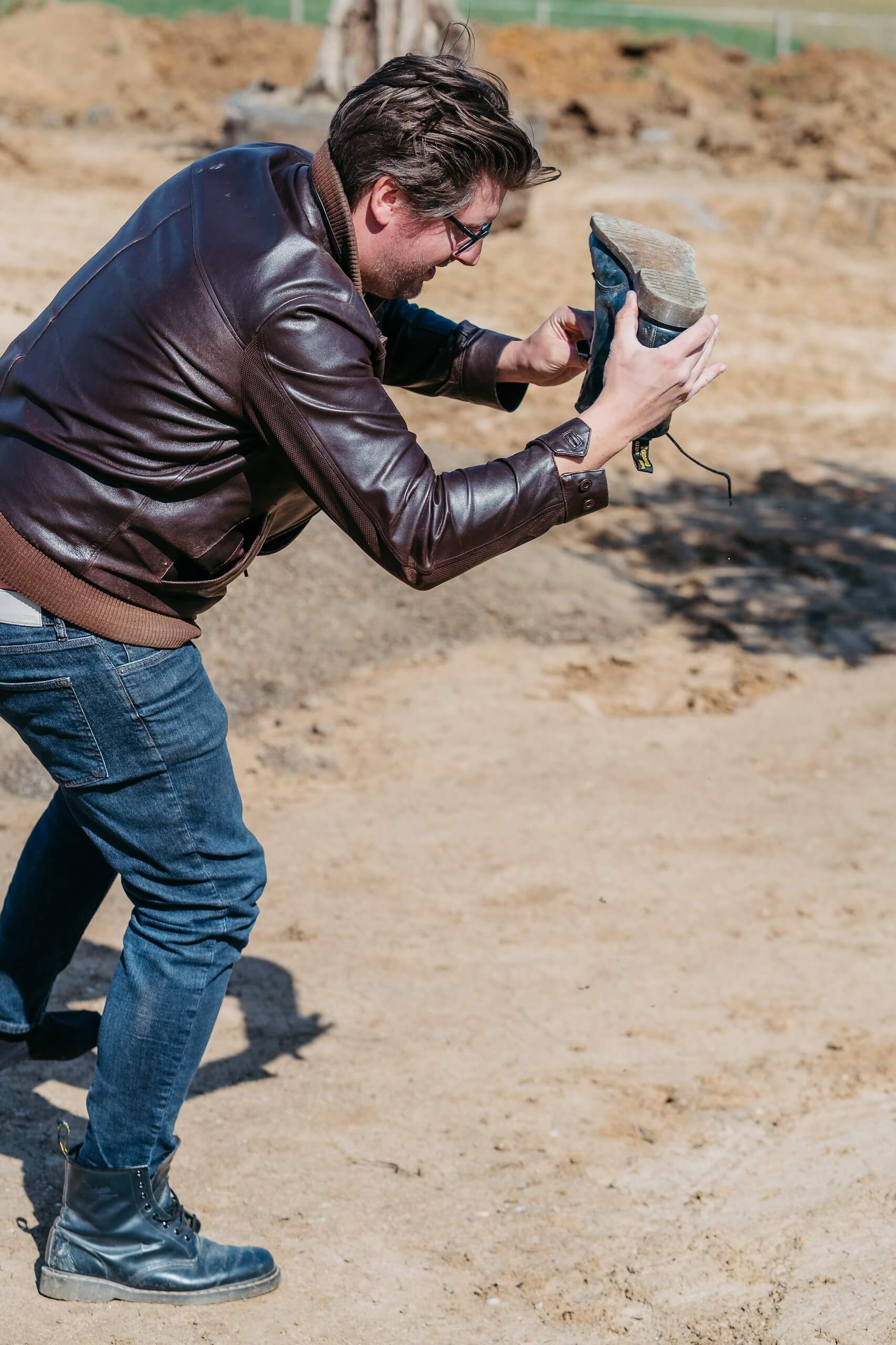 Eine Person in brauner Lederjacke prüft einen Schuh auf einer Baustelle. Vorbereitungen zur Traumhochzeitslocation.